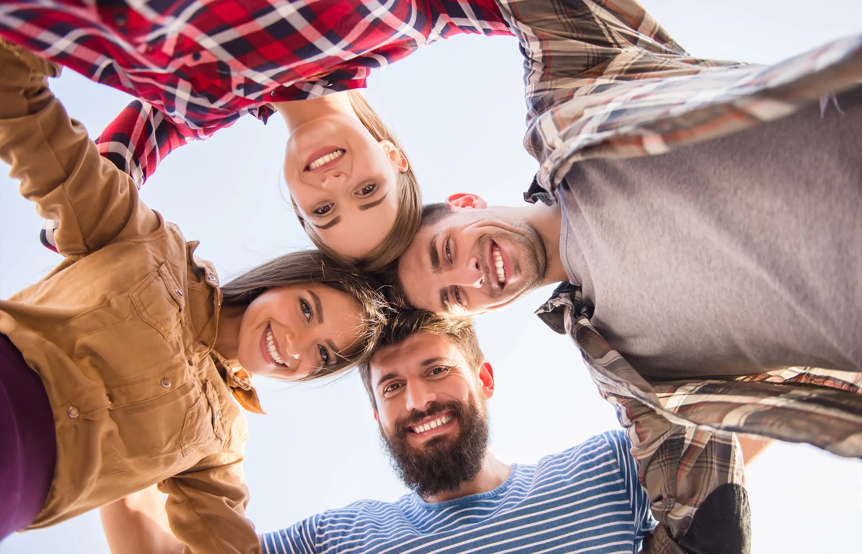 4 junge Menschen Kopf an Kopf aneinander gelehnt, lächeln in die Kamera.