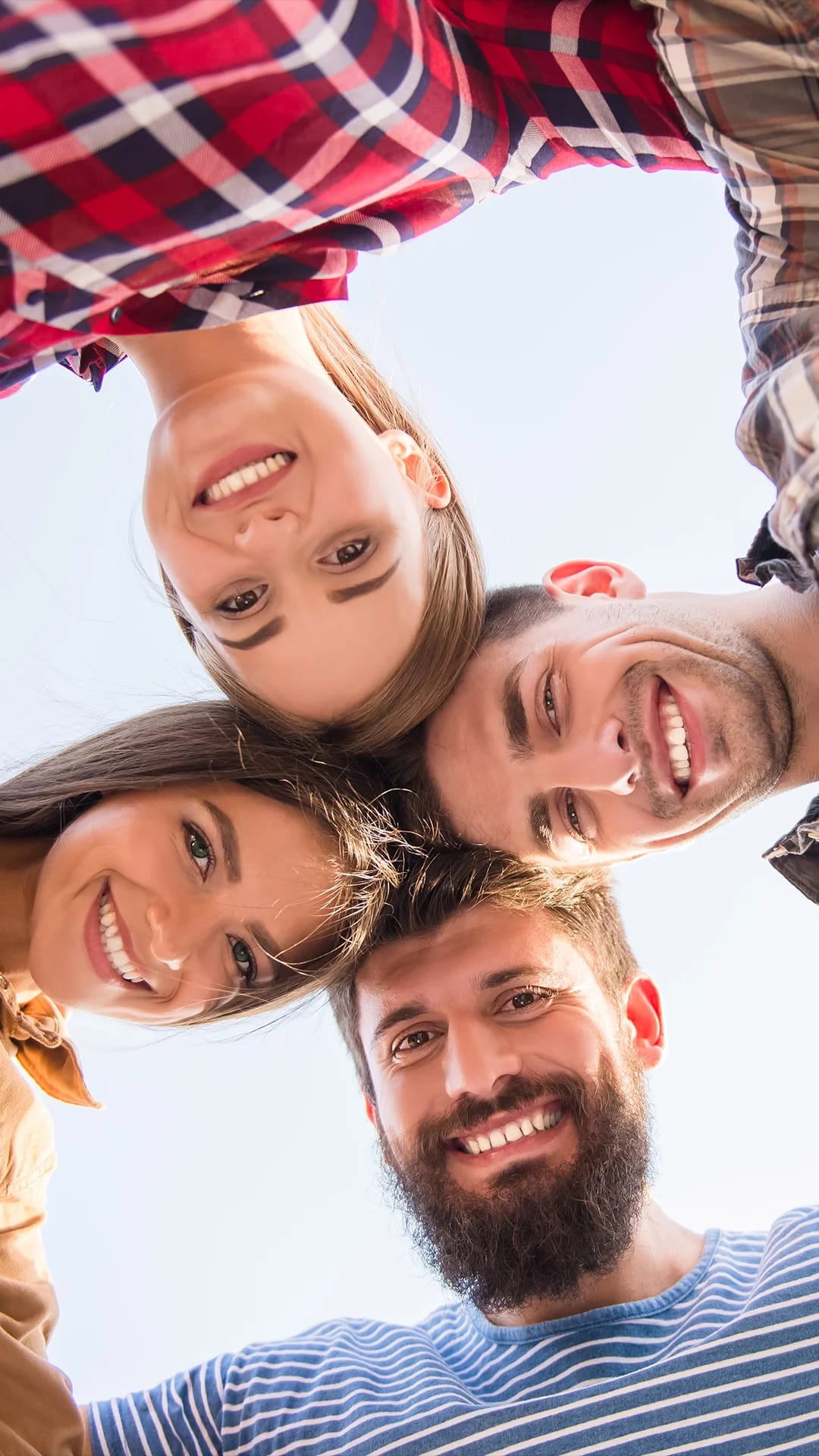 4 junge Menschen Kopf an Kopf aneinander gelehnt, lächeln in die Kamera.