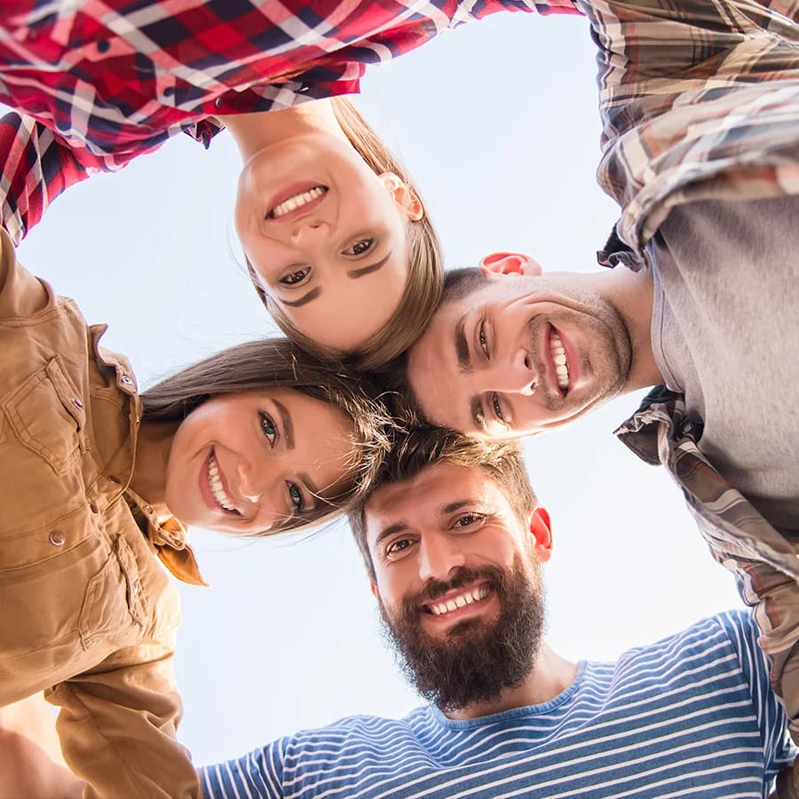 4 junge Menschen Kopf an Kopf aneinander gelehnt, lächeln in die Kamera.